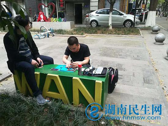 工程師在街邊石板凳為顧客維修手機(jī)。